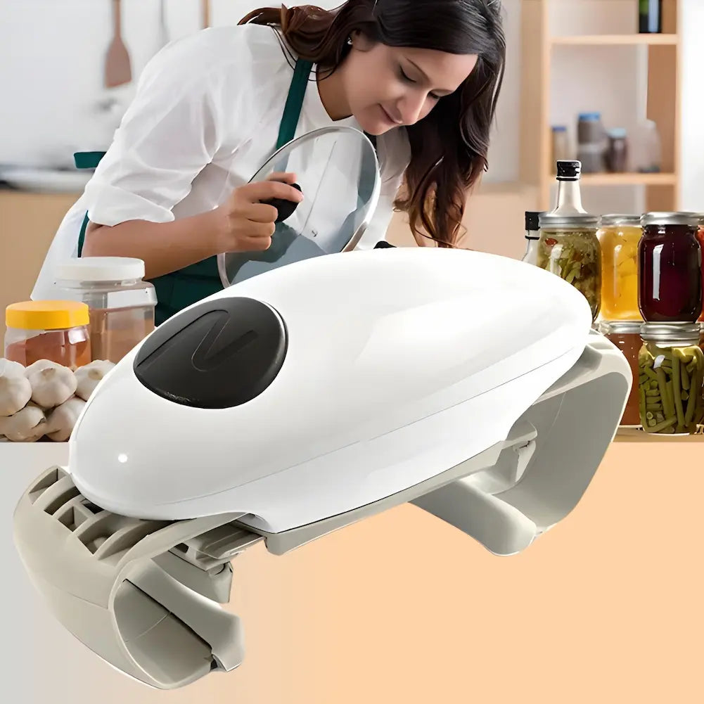 A imagem mostra uma mulher na cozinha, vestindo um avental, enquanto segura uma tampa de panela. Em primeiro plano, há um abridor de potes automático branco com detalhes cinza e um botão preto. Ao fundo, há vários potes de vidro contendo diferentes tipos de conservas e ingredientes.